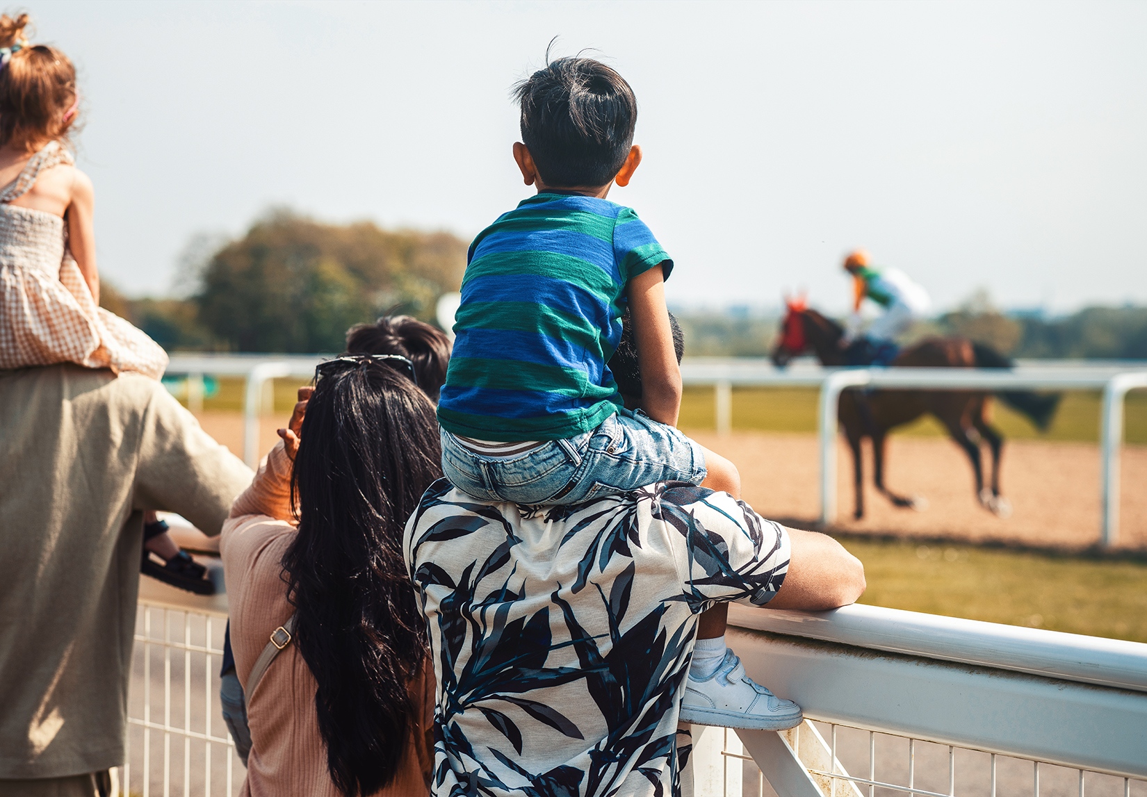 a boy sitting on his dad's shoulders watching a horse race